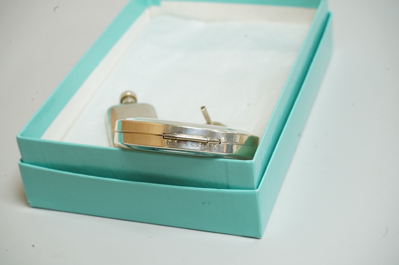 A small modern Tiffany & Co sterling scent flask, 44mm, together with a Tiffany & Co sterling compact, diameter 64mm and a small unmarked white metal funnel, with an associated Tiffany & Co box.